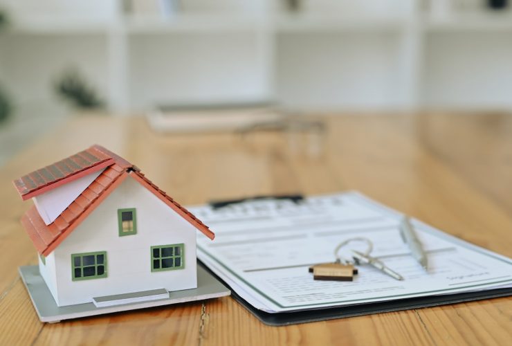 House model, keys and contract document on wooden table